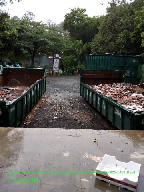 Na imagem estão duas caçambas de lixo na cor verde escuro com entulhos dentro. 